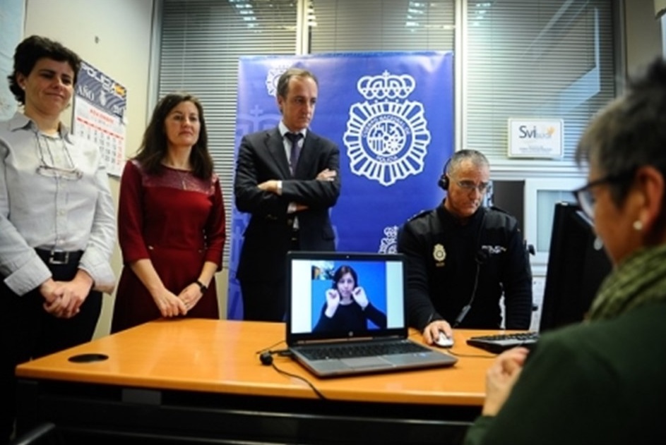 Un grupo de personas alrededor de una mesa y un ordenador en cuya pantalla aparece un itérprete de LSE.