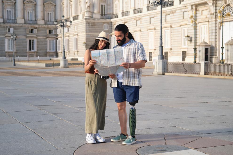 Una pareja mira un plano delante del Palacio Real. Uno tiene prótesis en una pierna