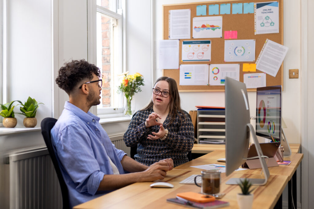 Coworkers Discussing Work in the Office. One is a man and the other one is a woman with down syndrome.