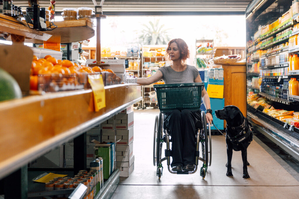Mujer usuaria de silla de ruedas con perro de asistencia en el supermercado.